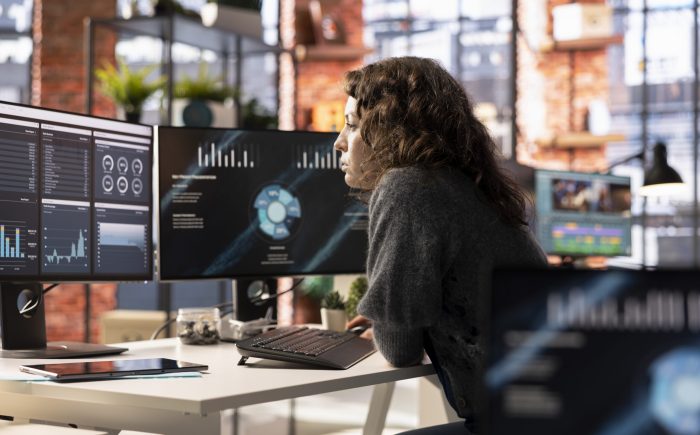 Young woman watching business conference infographics on computer screen, looking over statistics on online portfolio. Analyst in apartment looking at business presentation dashboard.