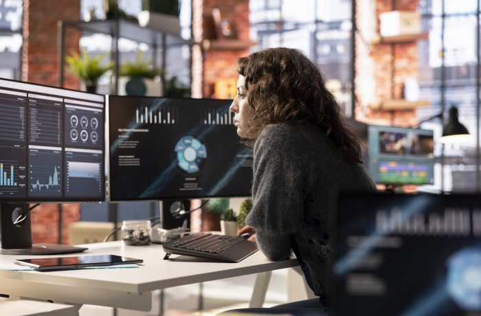 Young woman watching business conference infographics on computer screen, looking over statistics on online portfolio. Analyst in apartment looking at business presentation dashboard.